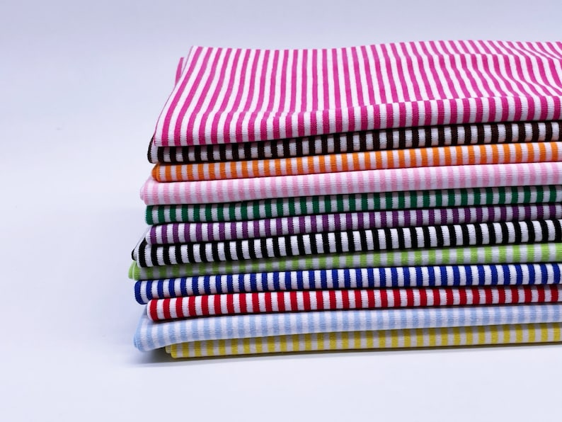 May include: A stack of striped fabric in various colors, including pink, orange, green, purple, blue, red, and yellow. The fabric is folded neatly and arranged in a vertical stack.