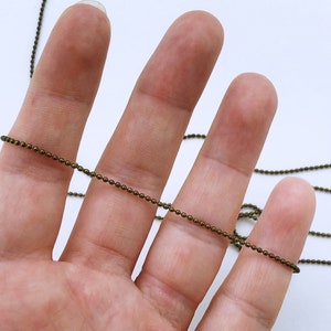May include: A close-up of a bronze chain, with a hand holding the chain in the foreground.
