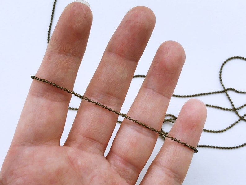May include: A close-up of a bronze chain, with a hand holding the chain in the foreground.