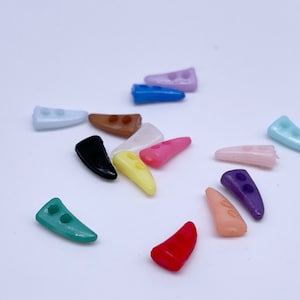 Puede incluir: Surtido de botones de plástico de colores en una variedad de formas y tamaños. Los botones tienen forma de cuerno con dos agujeros.