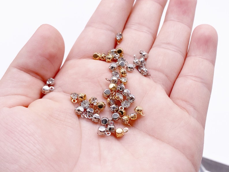 May include: A collection of gold and silver metal bead caps with clear rhinestones. The bead caps have a loop on the top for attaching to jewelry.