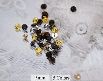 May include: Assortment of 5mm metal buttons in five colors: gold, silver, black, brown, and copper. The buttons have a swirl design and are displayed on a white lace background.