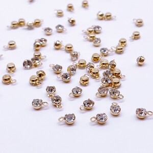 May include: A scattering of gold-toned metal charms with clear crystal rhinestones. Each charm has a small loop for attaching to jewelry or other crafts.