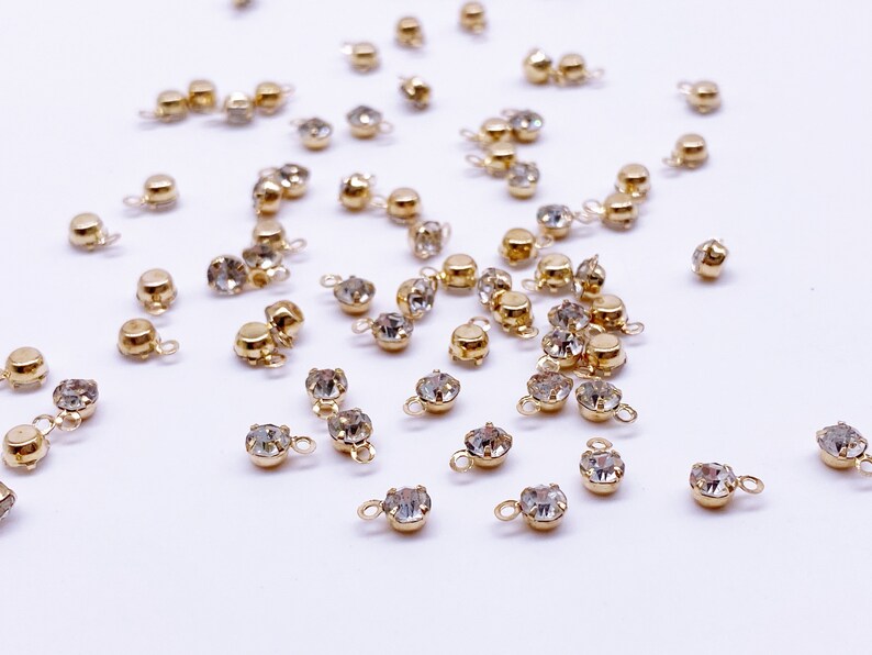 May include: A scattering of gold-toned metal charms with clear crystal rhinestones. Each charm has a small loop for attaching to jewelry or other crafts.