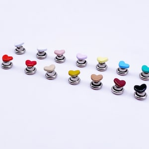 May include: Assortment of heart-shaped metal studs in various colours, including red, pink, yellow, blue, green, black, and brown. The studs are attached to a silver base.