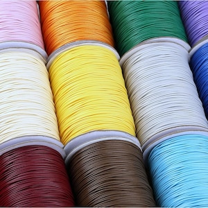 May include: Spools of colorful waxed cotton cord, perfect for crafting and jewelry making. The cords are wound around cardboard spools and come in a variety of colors, including pink, orange, yellow, green, white, brown, blue, and red.