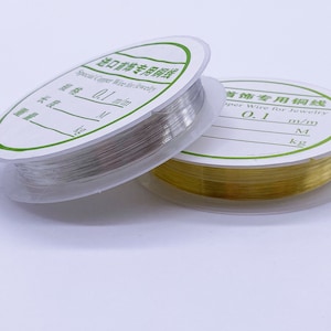 May include: Two spools of wire for jewelry making. One spool is silver and the other is gold. The spools are labeled with the text "Special Copper Wire for Jewelry" and "Copper Wire for Jewelry". The text also includes the measurements "0.1 mm/m" and "0.1 m/m".