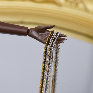 May include: Five different chain necklaces in gold, silver, and black metal. The chains are all the same length and are held in a hand.