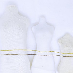 May include: Three white fabric mannequins of different sizes with a gold and brown chain wrapped around their waists.