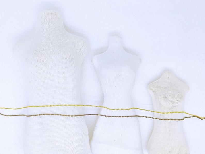 May include: Three white fabric mannequins of different sizes with a gold and brown chain wrapped around their waists.