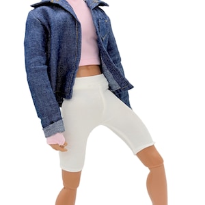 May include: A doll dressed in a denim jacket, pink turtleneck crop top, and white cycling shorts. The doll is also wearing white trainers with black socks. The outfit is a casual, modern style.