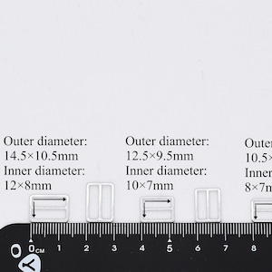 May include: Four silver metal slider buckles of different sizes. The buckles are arranged from largest to smallest. The outer diameter of the largest buckle is 14.5 x 10.5 mm, and the inner diameter is 12 x 8 mm. The outer diameter of the second largest buckle is 12.5 x 9.5 mm, and the inner diameter is 10 x 7 mm. The outer diameter of the third largest buckle is 10.5 x 9 mm, and the inner diameter is 8 x 7 mm. The smallest buckle is 7 x 5 mm, and the inner diameter is 5 x 3 mm.