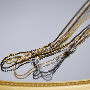 May include: A close-up of multiple chains of different colors and metals. The chains are made of small, round beads and are arranged in a fan shape. The chains are reflected in a mirror surface.