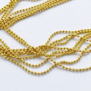 May include: A close-up of a gold ball chain, a type of jewelry chain made of small, round metal balls connected by links.