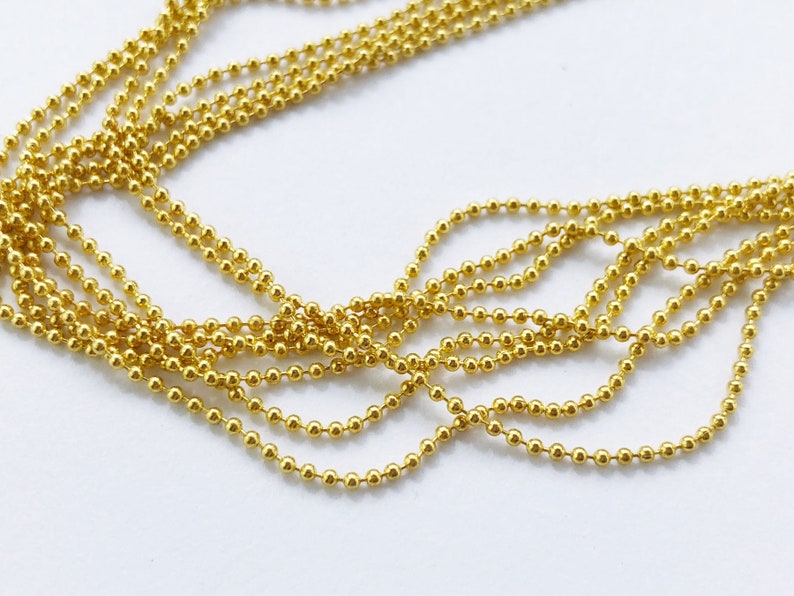 May include: A close-up of a gold ball chain, a type of jewelry chain made of small, round metal balls connected by links.