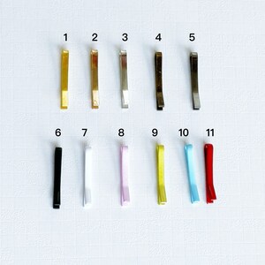 May include: Eleven hair clips in different colours, including gold, silver, black, white, pink, yellow, blue, and red. The clips are numbered 1 through 11.