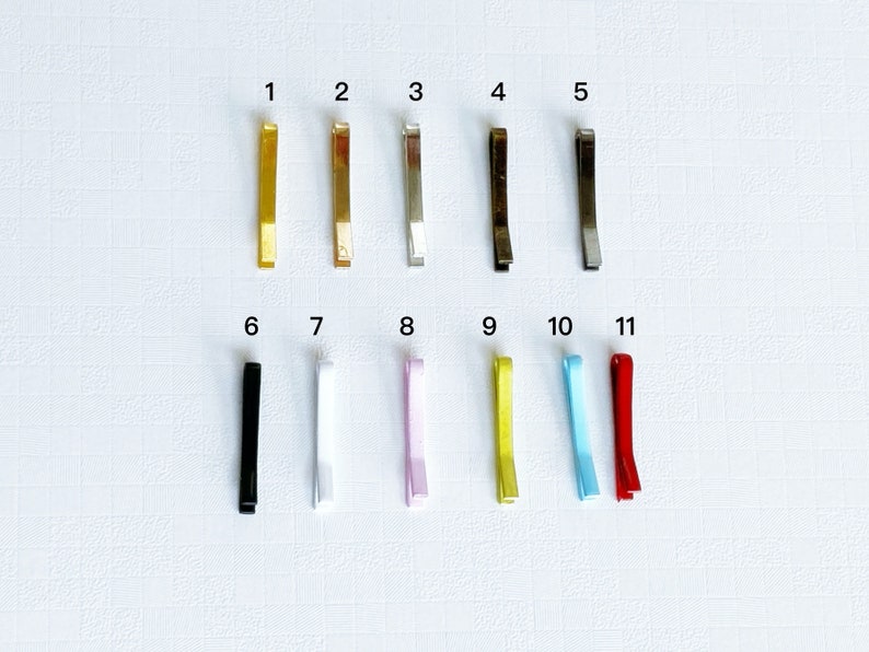May include: Eleven hair clips in different colours, including gold, silver, black, white, pink, yellow, blue, and red. The clips are numbered 1 through 11.