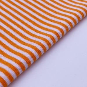 May include: Orange and white striped fabric with a ribbed texture. The fabric is folded in half and the stripes are running diagonally.