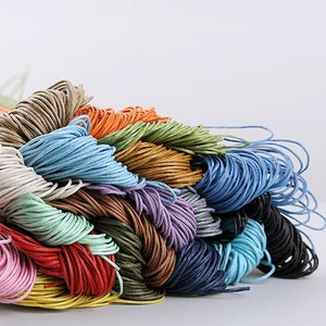 May include: A pile of colorful waxed cotton cords in various shades of blue, green, brown, red, orange, and pink. The cords are arranged in a random pattern, creating a visually appealing and textured display.