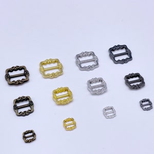 Könnte beinhalten: Sortiment an Metallschnallen in verschiedenen Größen und Ausführungen, darunter Gold, Silber und Schwarz. Die Schnallen haben ein verziertes Design mit quadratischer Form und einem Mittelbalken.