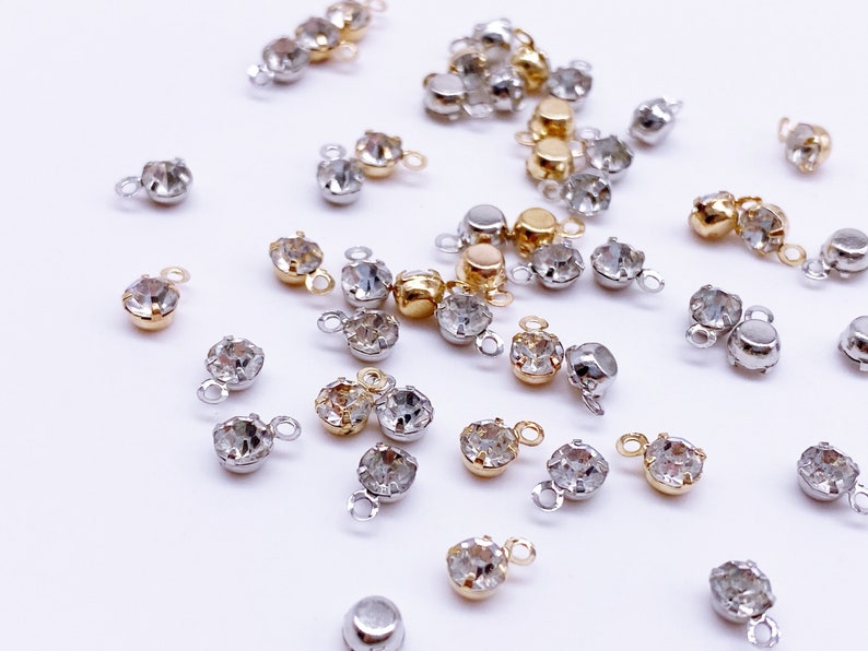 May include: Assortment of clear crystal rhinestone connectors with gold and silver settings. The connectors have a loop on the top for attaching to jewelry or other crafts.