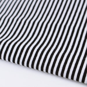 May include: Black and white striped fabric with a smooth texture. The fabric is folded in half and the stripes are running vertically.