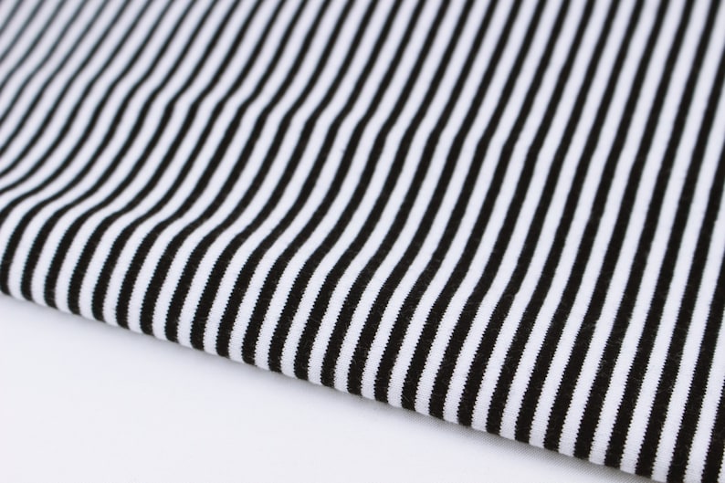 May include: Black and white striped fabric with a smooth texture. The fabric is folded in half and the stripes are running vertically.