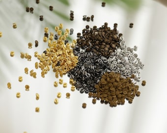 May include: A close-up of a variety of small metal buttons in gold, silver, and bronze colors. The buttons are scattered on a white surface.