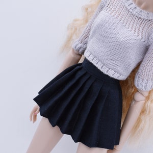May include: A black pleated skirt with a white knitted sweater. The skirt is short and has a high waist.