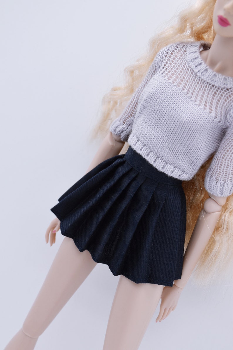 May include: A black pleated skirt with a white knitted sweater. The skirt is short and has a high waist.