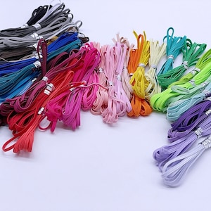 May include: Assortment of colorful elastic bands in various shades, including red, pink, blue, green, and purple. The bands are arranged in a semi-circle on a white surface.