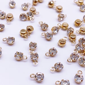 May include: A collection of gold-toned metal charms with clear crystal rhinestones. Each charm features a small loop for attaching to jewelry or other crafts.
