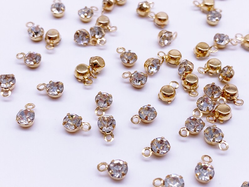 May include: A collection of gold-toned metal charms with clear crystal rhinestones. Each charm features a small loop for attaching to jewelry or other crafts.