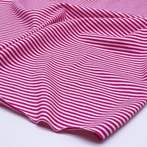 May include: Pink and white striped fabric with a soft, stretchy texture. The fabric is folded and draped, showing the pattern and texture.