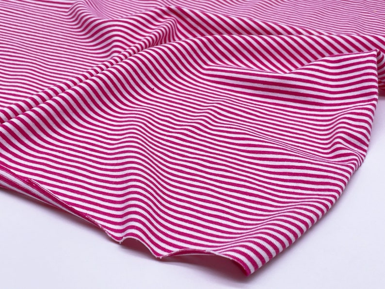 May include: Pink and white striped fabric with a soft, stretchy texture. The fabric is folded and draped, showing the pattern and texture.