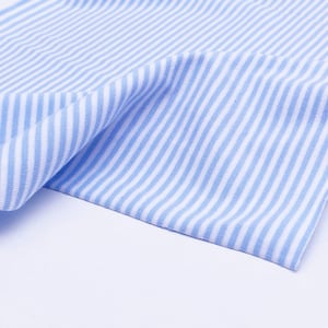 May include: A close-up of a blue and white striped fabric. The fabric is folded and has a soft, textured appearance.