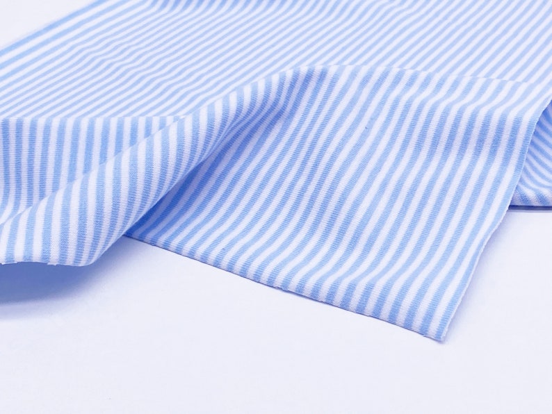 May include: A close-up of a blue and white striped fabric. The fabric is folded and has a soft, textured appearance.