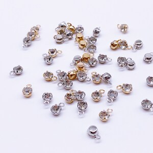 May include: A collection of clear crystal rhinestones with gold and silver settings. Each rhinestone has a small loop on the back for attaching to jewelry or other crafts.