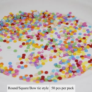 May include: A white plate filled with colorful round and square buttons. The buttons are in various colors, including red, yellow, blue, green, and pink. The text on the plate reads "Round/Square/Bow tie style 50 pcs per pack".