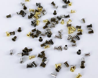 May include: A collection of small metal eyelets in various colors, including gold, silver, and bronze, scattered on a white surface. These eyelets are cylindrical with a flared top, suitable for crafting and DIY projects.