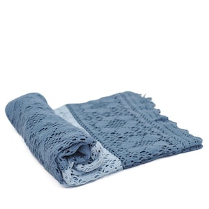 May include: A rolled-up, open-weave, blue crochet blanket with a fringed edge. The blanket is a gradient of light to medium blue, with a detailed, geometric pattern. The blanket is made of soft, breathable material.