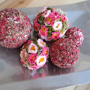 Op de afbeelding: Vijf decoratieve bollen, drie zijn bedekt met roze en rode bloemblaadjes en twee zijn bedekt met roze en witte bloemen.