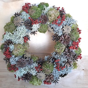 Op de afbeelding: Een kerstkrans gemaakt van mos, dennenappels en rode bessen. De krans is versierd met natuurlijke elementen en is perfect om een ​​rustieke charme toe te voegen aan uw kerstdecoratie.