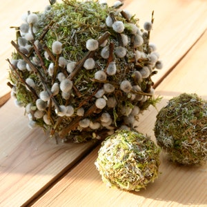 May include: Three decorative spheres made of moss and twigs. The largest sphere is decorated with white fluffy buds.