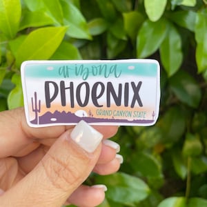 May include: A white sticker with a blue and orange design. The sticker says "Arizona Phoenix Grand Canyon State".