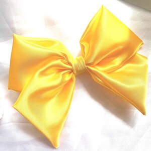 May include: A large yellow satin bow. The bow is tied in a classic shape with two loops and a centre knot.