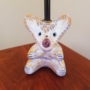 May include: A ceramic lamp base shaped like a white and yellow koala with large blue eyes. The koala is sitting on a wooden surface.