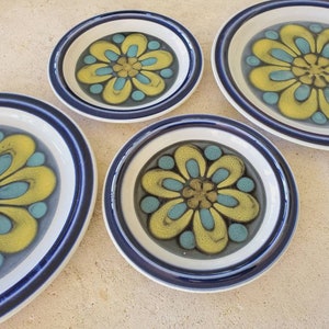 Puede incluir: Juego de cuatro platos de cerámica con borde azul y blanco y diseño floral amarillo y azul.