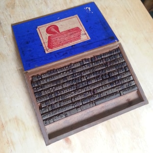 May include: A wooden box filled with metal letterpress printing blocks. The box has a blue lid with a label that reads "The White Metal Type Co.  All Sizes of Type  Made to Order  No. 1000  Moulds Always in Stock  New York City".