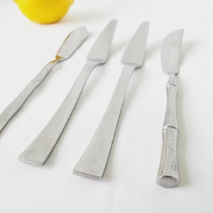 May include: Four silver butter knives with different handle styles. Three knives have plain handles, while one has a textured bamboo-style handle.